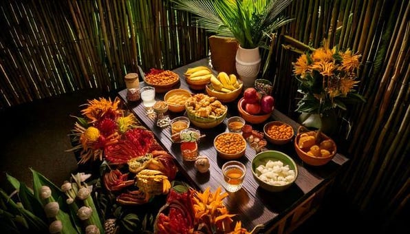 Altar tradicional de Hanal Pixan en Yucatán, decorado con diversos alimentos como frutas, dulces y platillos típicos, rodeado de flores y elementos naturales en un ambiente rústico de bambú. La mesa incluye jícaras, flores de cempasúchil y ofrendas, simbolizando la celebración y honra. a los difuntos en la cultura maya.